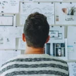 A man looking at the board and applying design thinking process with the printouts of product plans, wireframes, prototypes