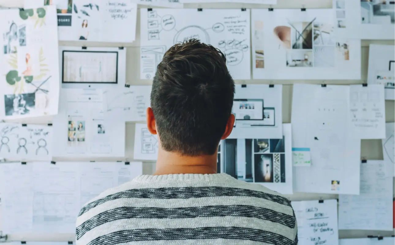 A man looking at the board and applying design thinking process with the printouts of product plans, wireframes, prototypes