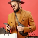 Man in a Brown Blazer Carrying Shopping Bags while Using His Cell Phone
