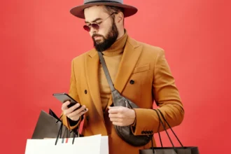 Man in a Brown Blazer Carrying Shopping Bags while Using His Cell Phone