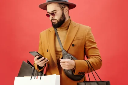 Man in a Brown Blazer Carrying Shopping Bags while Using His Cell Phone