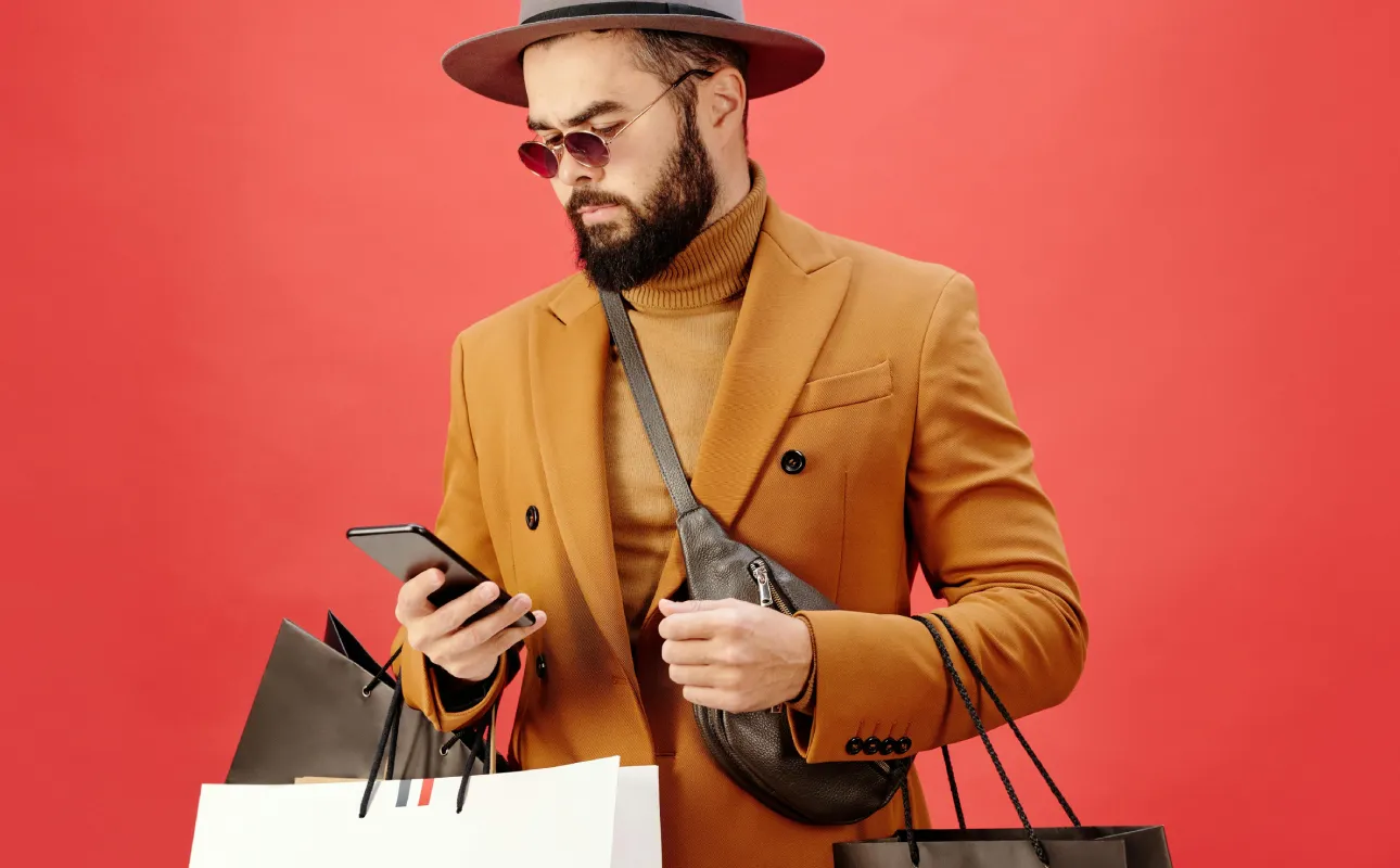 Man in a Brown Blazer Carrying Shopping Bags while Using His Cell Phone