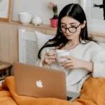 Woman Having Coffee And Using Laptop In Bed