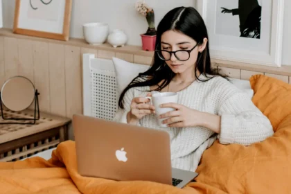 Woman Having Coffee And Using Laptop In Bed